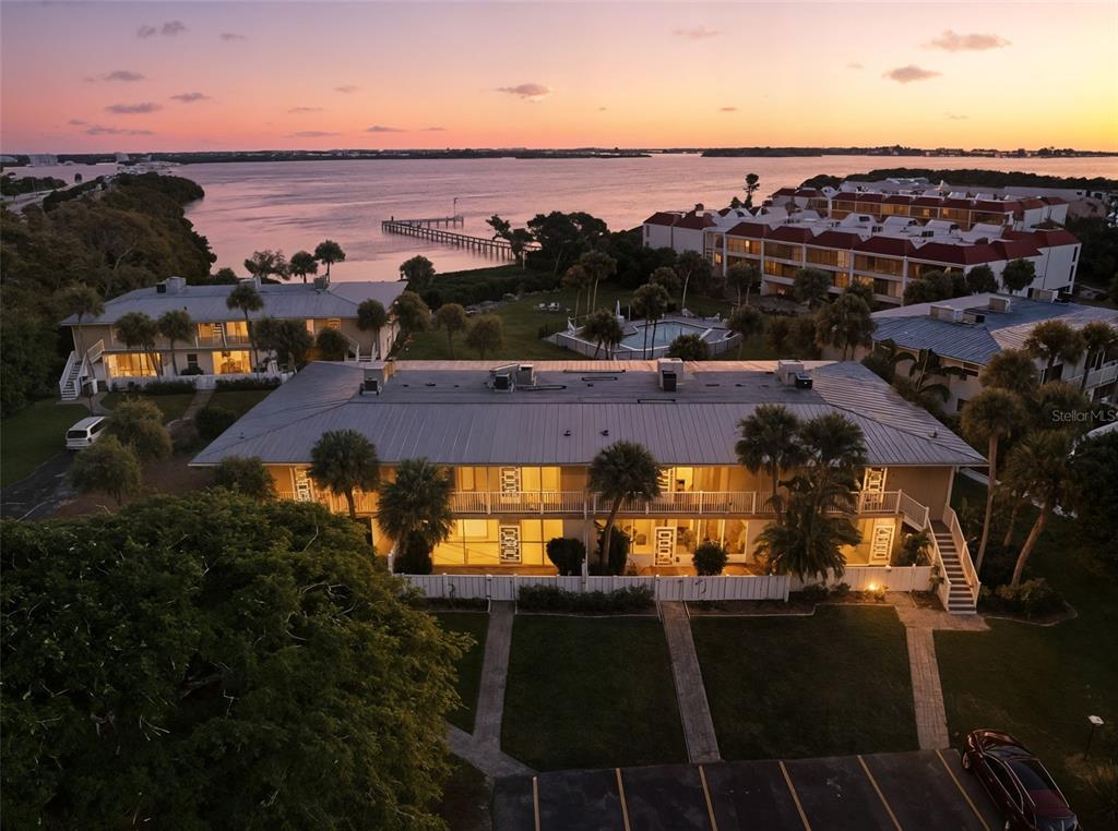 An aerial view shows a multi-story apartment building at sunset near a waterfront dock — 749 MANATEE AVENUE UNIT 749, HOLMES BEACH, FL