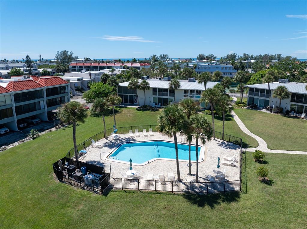 An aerial view shows a swimming pool surrounded by a fence, palm trees, and buildings — 749 MANATEE AVENUE UNIT 749, HOLMES BEACH, FL