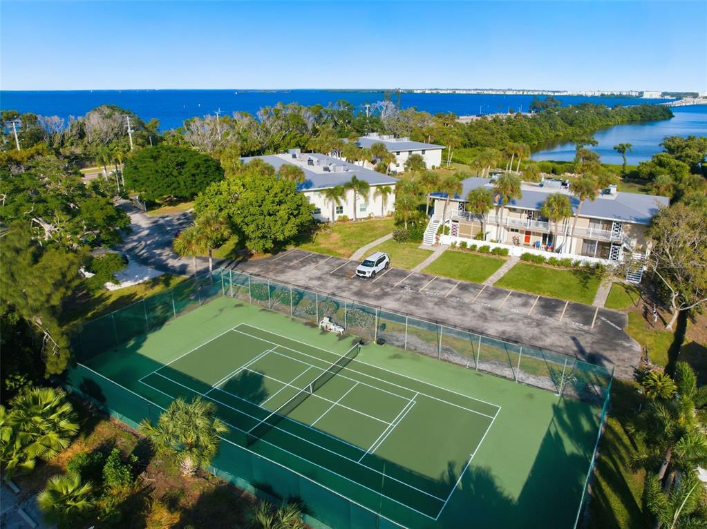An aerial view shows a tennis court, a parking lot, and two apartment buildings near water — 749 MANATEE AVENUE UNIT 749, HOLMES BEACH, FL