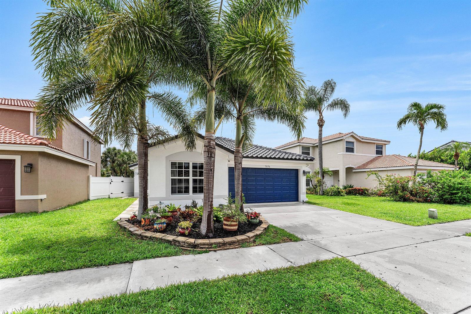 A single-story house with a blue garage door and palm trees in the front yard — 7076 Middlebury Drive, Boynton Beach FL 33436, BOYNTON BEACH, FL