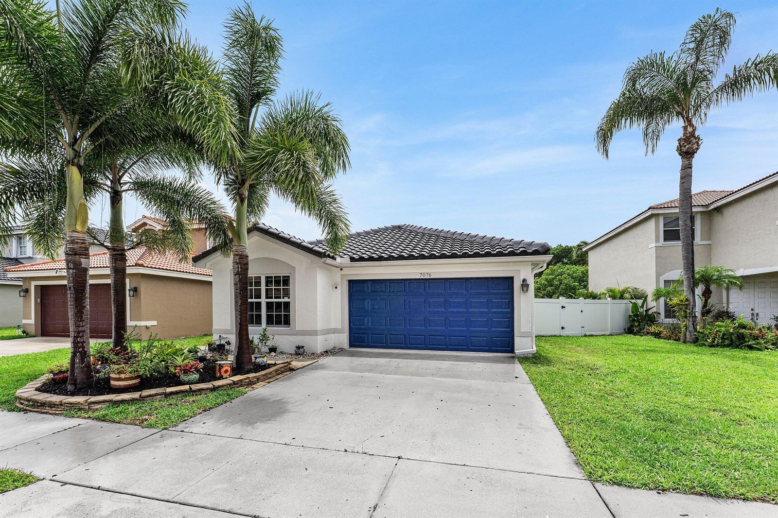 A single-story house with a blue garage door, palm trees, and a concrete driveway — 7076 Middlebury Drive, Boynton Beach FL 33436, BOYNTON BEACH, FL
