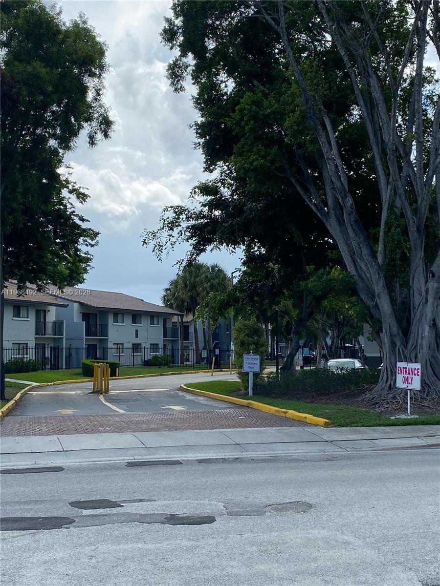 An entrance to a residential complex features a paved driveway, mature trees, and signage — 7030 NW 179th St # 205, Hialeah FL 33015, HIALEAH, FL