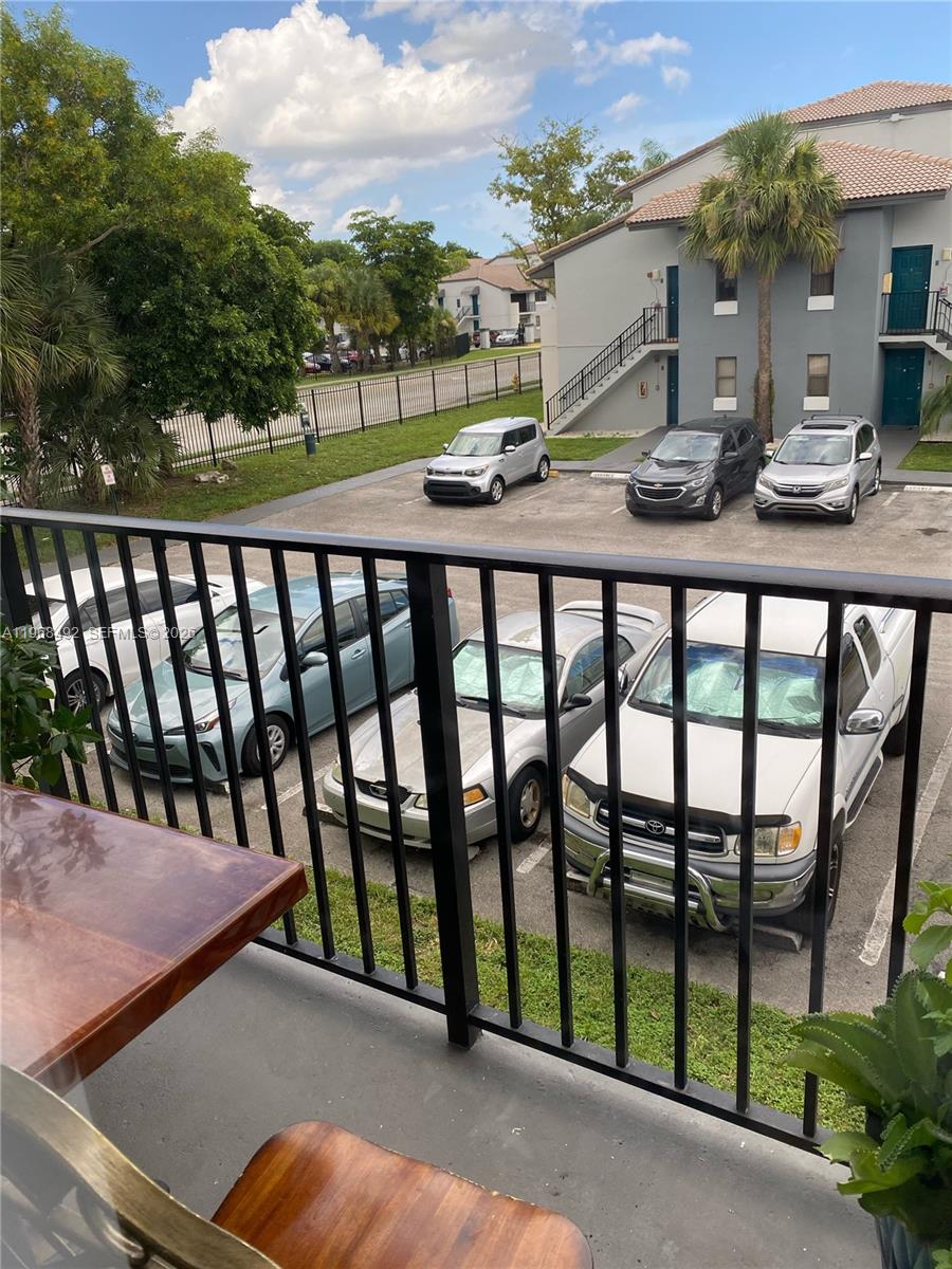 A view from a balcony overlooking a parking lot with several cars and apartment buildings — 7030 NW 179th St # 205, Hialeah FL 33015, HIALEAH, FL