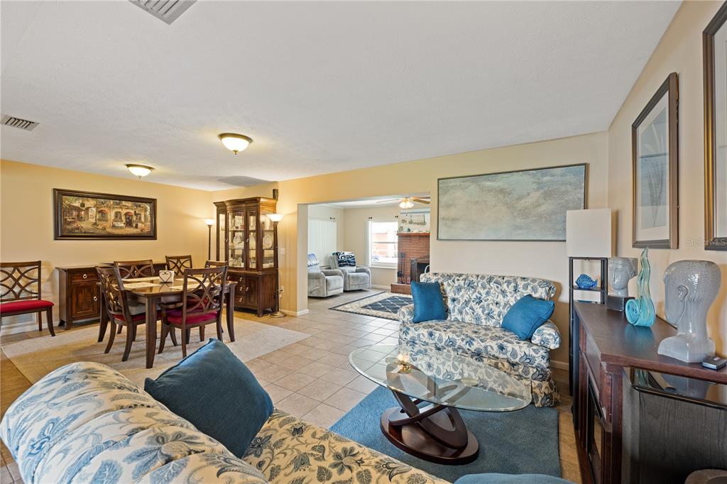A living room and dining area feature tile floors, floral furniture, and a brick fireplace — 415 HIAWATHA AVENUE, INVERNESS, FL