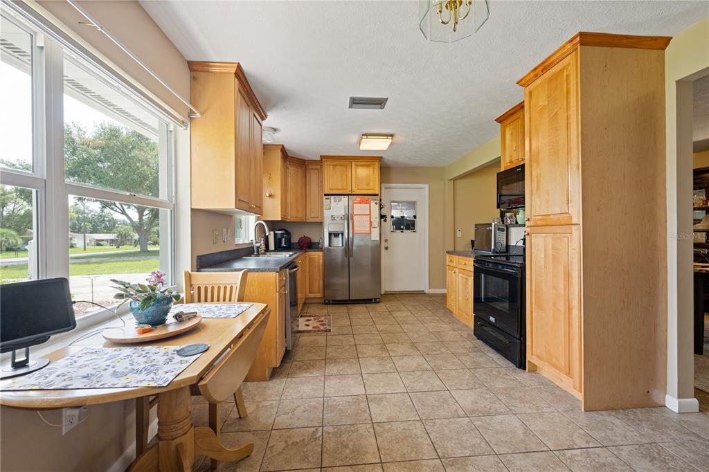 A kitchen features light wood cabinets, black appliances, a tile floor, and a dining table — 415 HIAWATHA AVENUE, INVERNESS, FL
