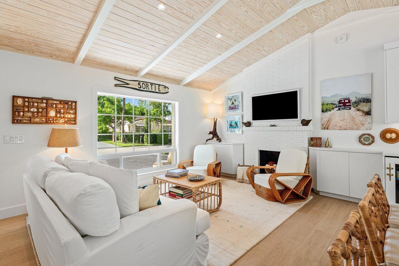 A bright living room features a white brick fireplace, vaulted wood ceiling, and rattan furniture — 11 Hersey Drive, Ocean Ridge FL 33435, OCEAN RIDGE, FL