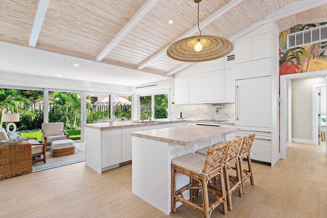 A bright kitchen features white cabinetry, a stone island with rattan stools, and vaulted ceilings — 11 Hersey Drive, Ocean Ridge FL 33435, OCEAN RIDGE, FL