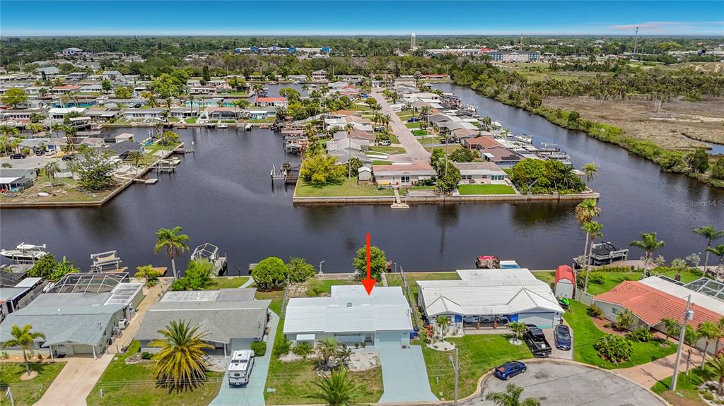 An aerial view shows a light-colored house with a red arrow pointing to its roof — 12524 5TH ISLE, HUDSON, FL