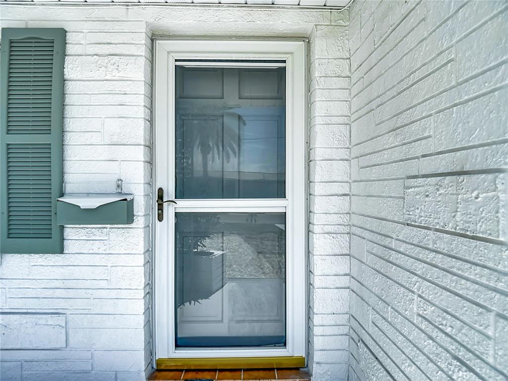A white storm door is mounted on a white painted brick exterior wall — 12524 5TH ISLE, HUDSON, FL