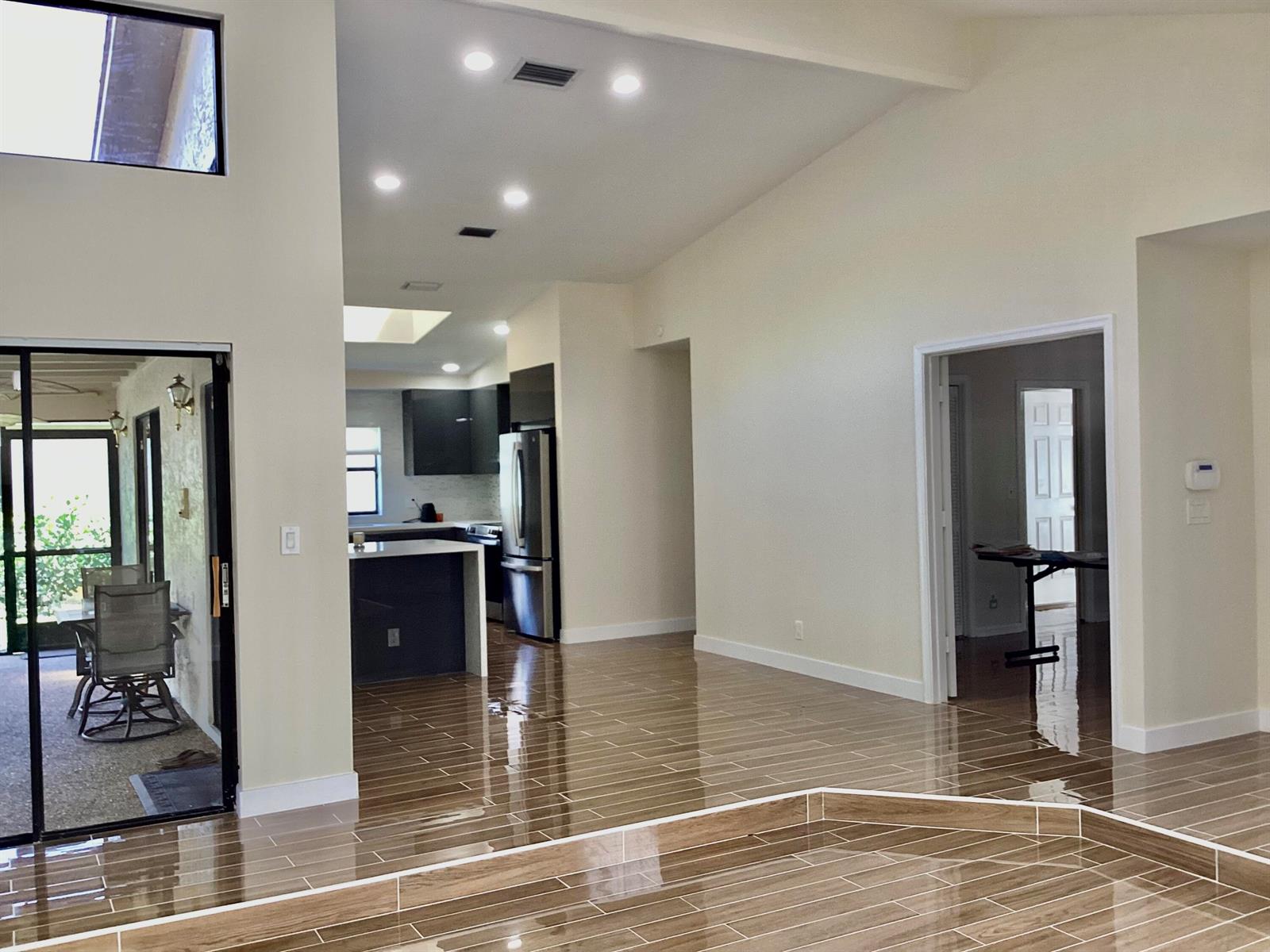 A bright, open-concept living area features glossy wood-look tile flooring and a modern kitchen — 8895 Old Pine Road, Boca Raton FL 33433, BOCA RATON, FL