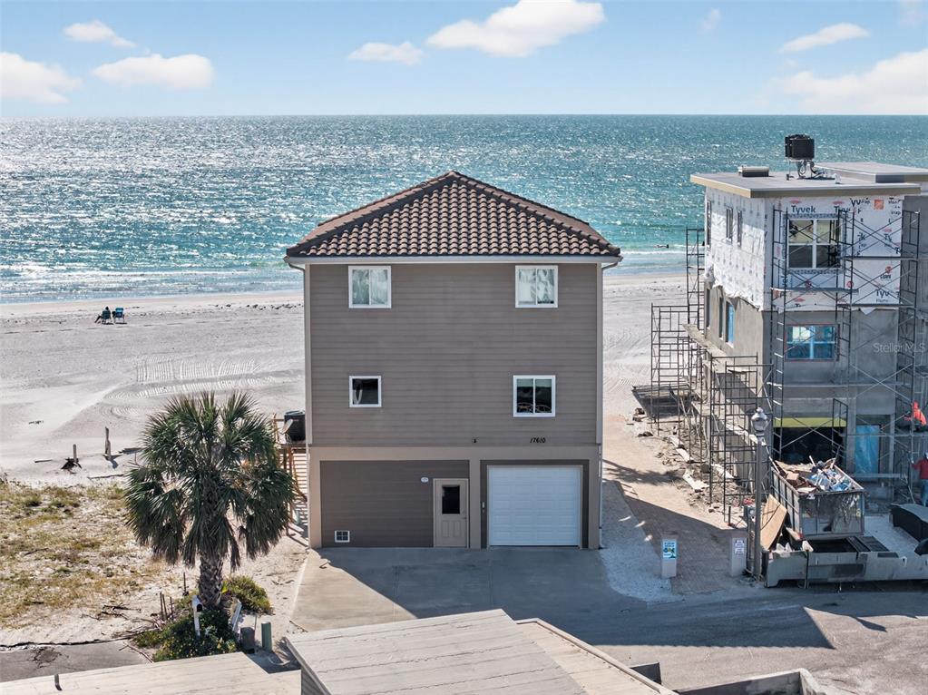 A three-story beach house stands beside a construction site on a sandy shore — 17610 LEE AVENUE, REDINGTON SHORES, FL