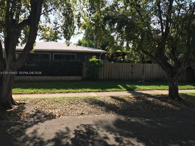 A single-story house with a wooden fence stands behind a grassy lawn and trees — 11400 NE 4 Ave # 2, Miami FL 33161, MIAMI, FL