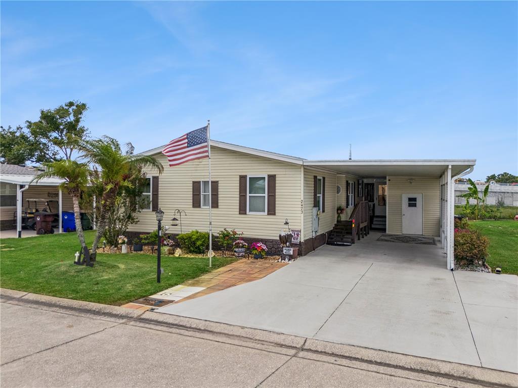A single-story manufactured home with light siding, a front lawn, and an attached carport — 2473 INDEPENDENCE LANE, ST CLOUD, FL