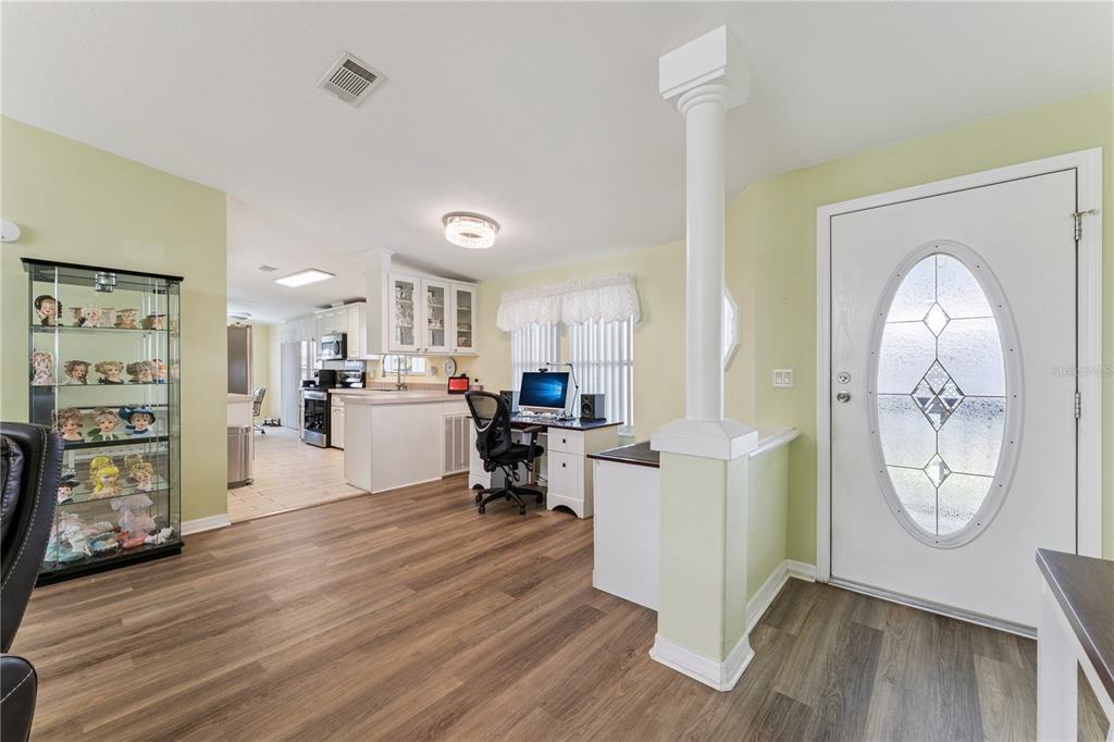 An open-concept room features light green walls, wood-look flooring, a desk area, and a front door — 2473 INDEPENDENCE LANE, ST CLOUD, FL