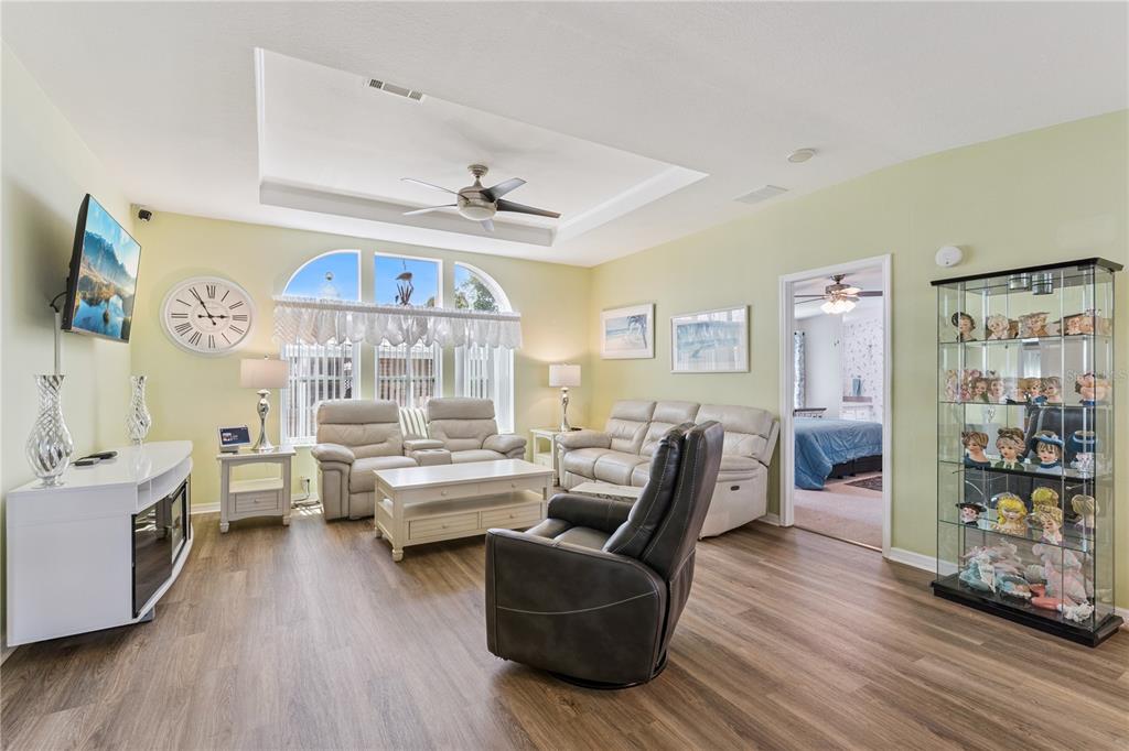 A living room features light green walls, wood-look flooring, a tray ceiling, and furniture — 2473 INDEPENDENCE LANE, ST CLOUD, FL