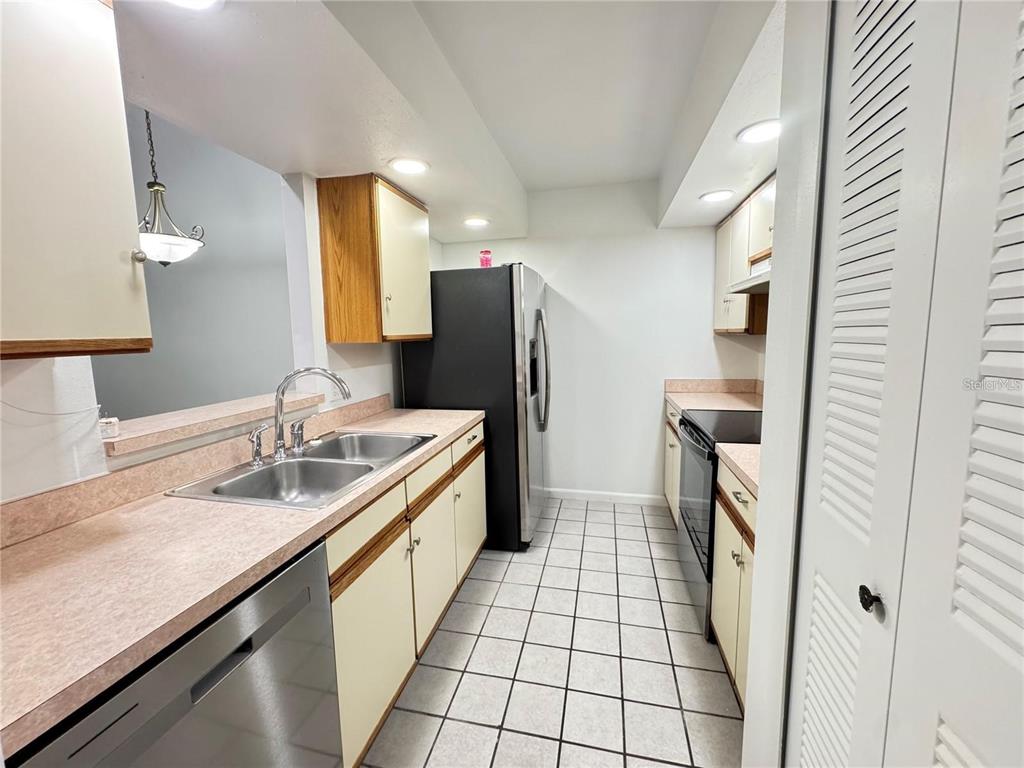 A galley kitchen features light-colored cabinets, laminate countertops, stainless steel appliances, and tiled flooring — 497 CLUB DRIVE, WINTER SPRINGS, FL