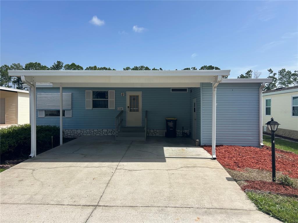 A light blue manufactured home features a concrete driveway, a carport, and a front entrance — 230 SUE AVENUE, DAVENPORT, FL