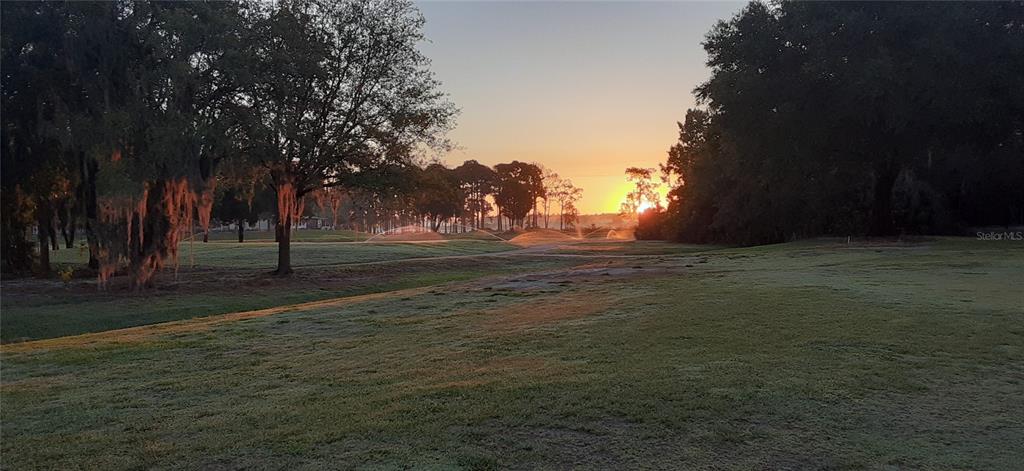 A view of a grassy golf course at sunrise with trees and active lawn sprinklers — 230 SUE AVENUE, DAVENPORT, FL