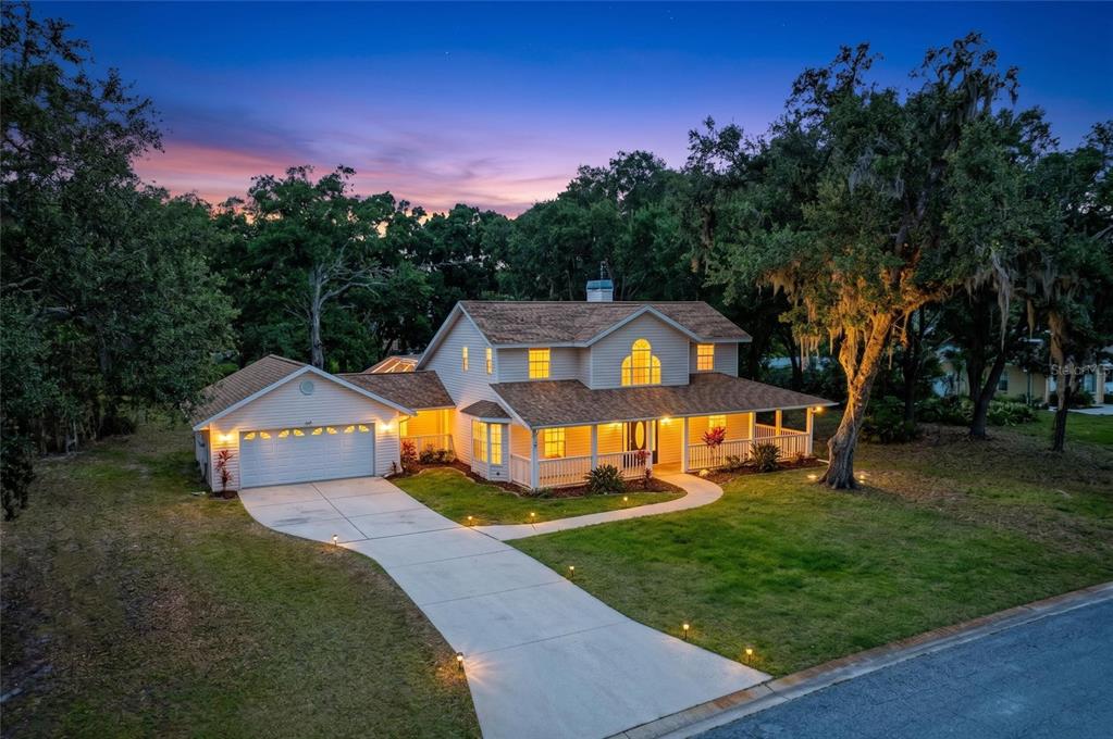 An aerial view of a two-story suburban house with a wrap-around porch at dusk — 518 129TH STREET NE, BRADENTON, FL