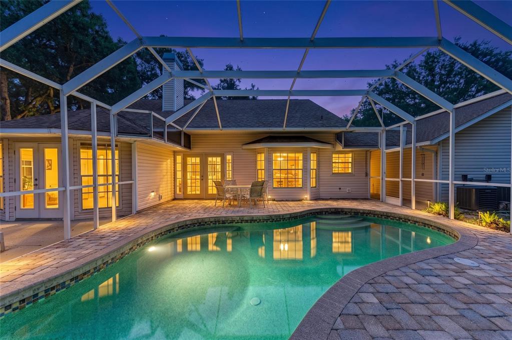 A swimming pool sits on a paved patio inside a screened-in lanai at dusk — 518 129TH STREET NE, BRADENTON, FL