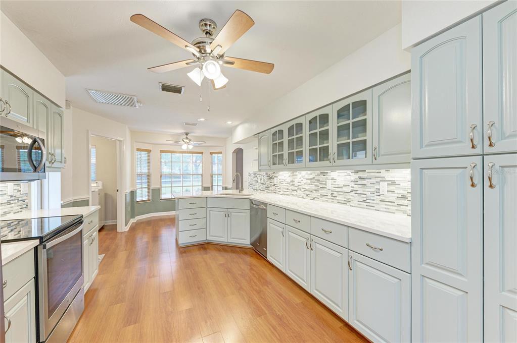 A kitchen features light blue cabinets, white countertops, a tile backsplash, and wood-look flooring — 518 129TH STREET NE, BRADENTON, FL