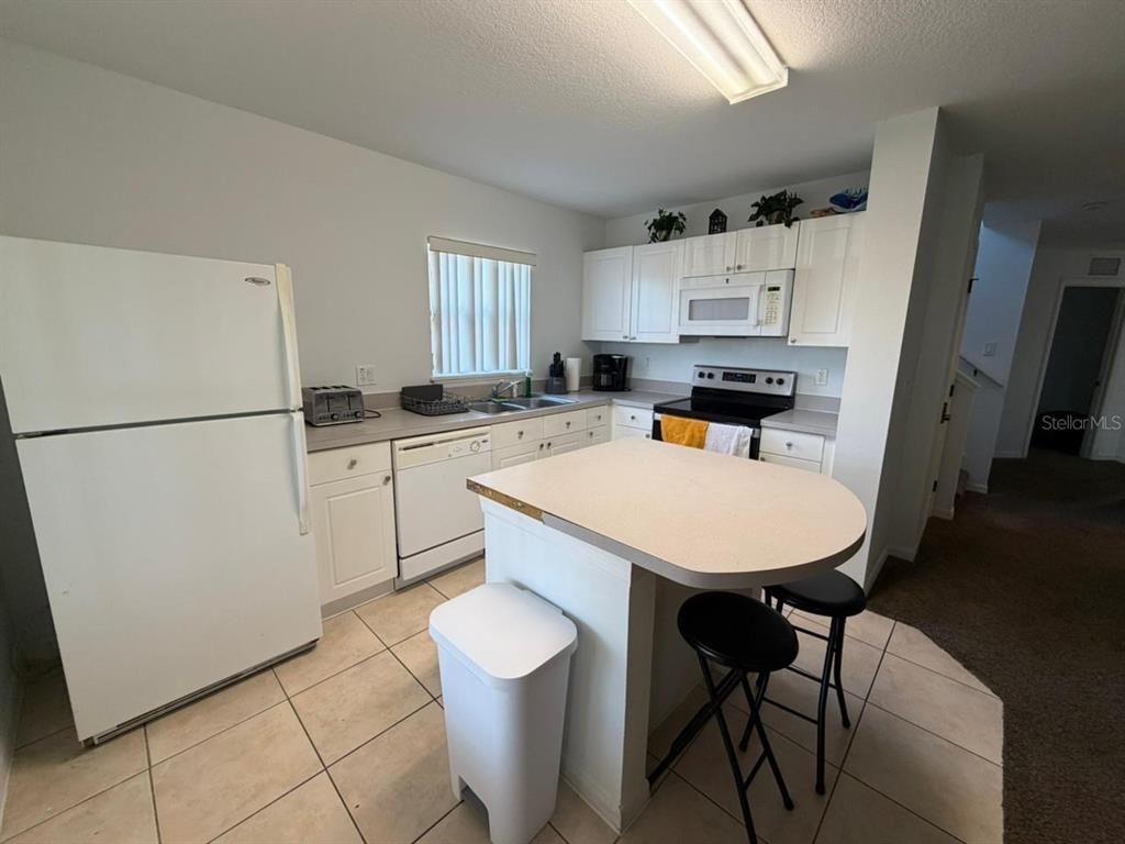 A kitchen features white cabinets, white appliances, a central island with stools, and tile flooring — 2714 CLUB CORTILE CIRCLE, KISSIMMEE, FL