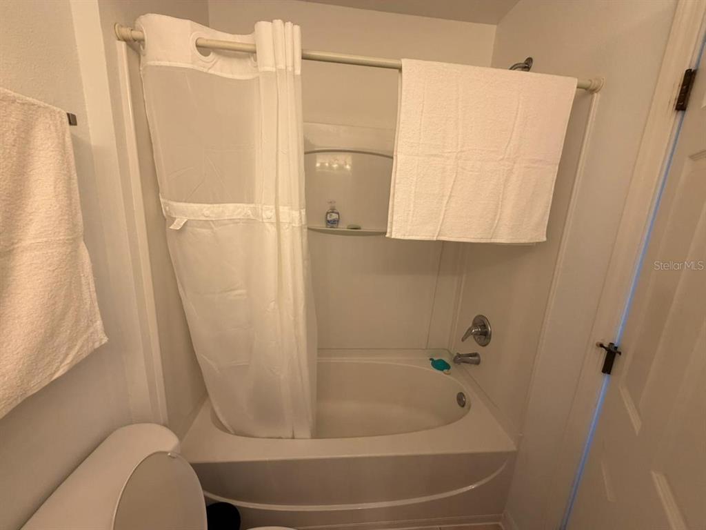 A bathroom features a white bathtub with a shower curtain and a wall-mounted towel — 2714 CLUB CORTILE CIRCLE, KISSIMMEE, FL