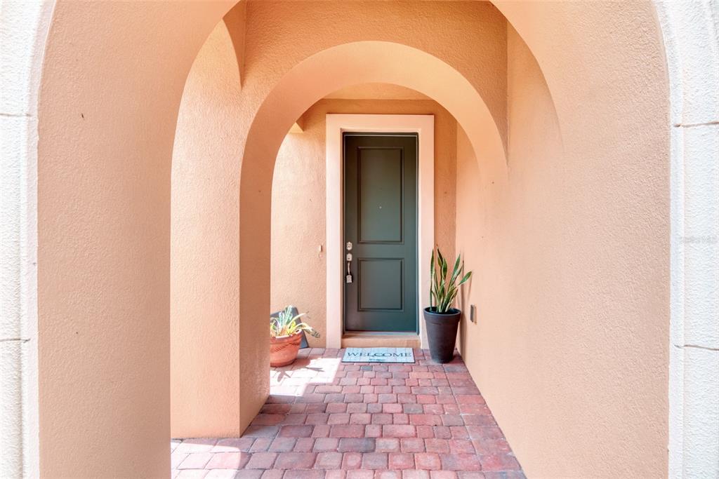 A dark green front door is set within a peach-colored arched entryway with brick flooring — 1390 HARBOR RIDGE DRIVE, KISSIMMEE, FL