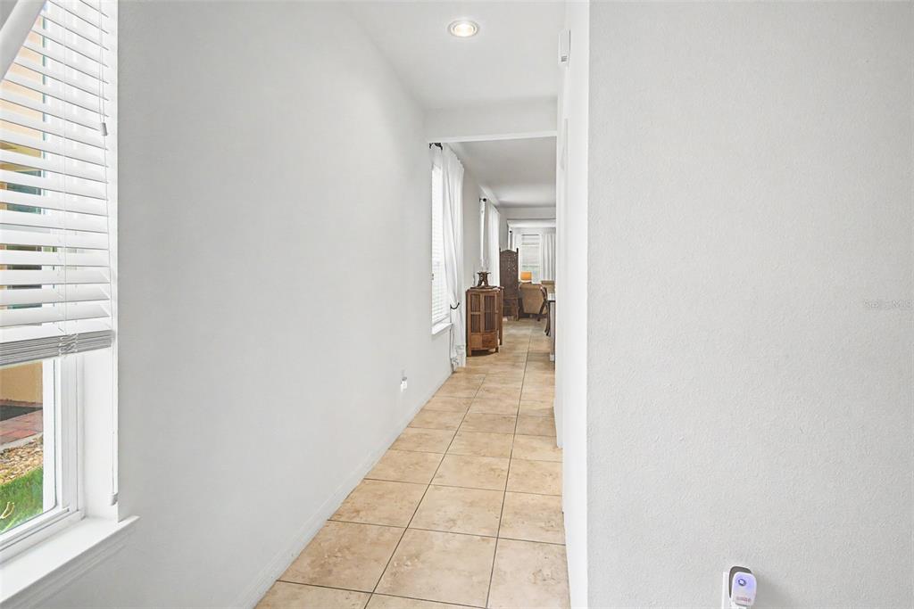 A hallway with light-colored walls and tan tile flooring leads toward an open living area — 1390 HARBOR RIDGE DRIVE, KISSIMMEE, FL
