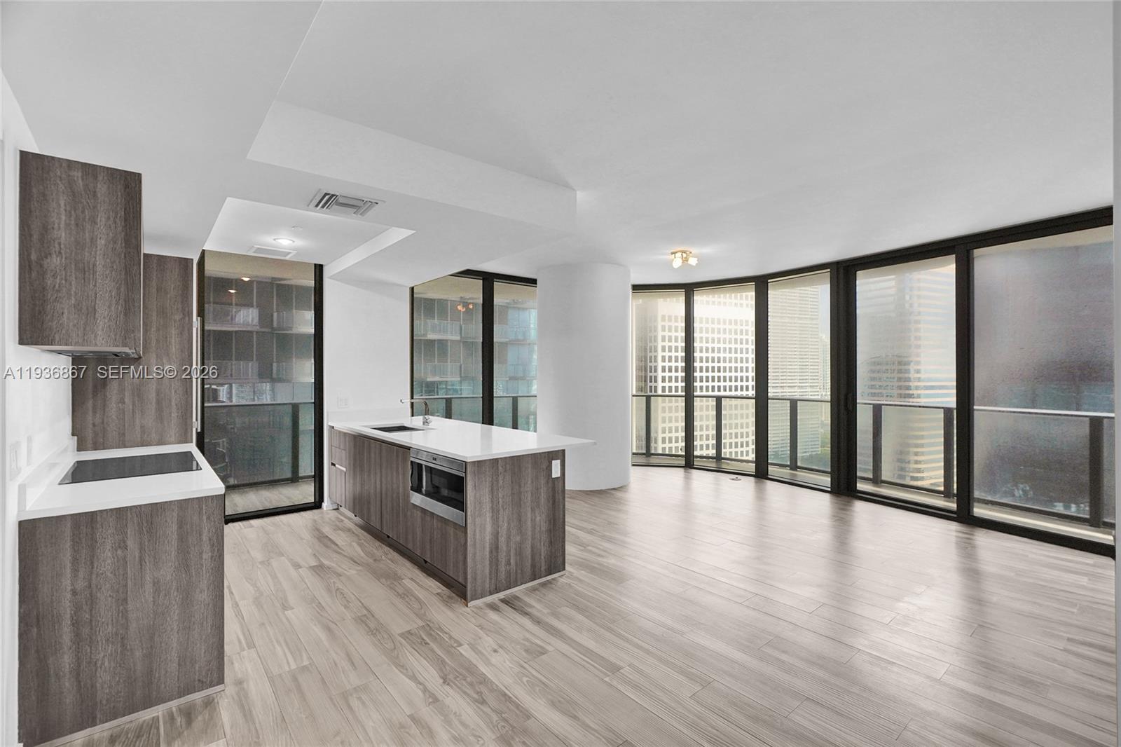 A modern kitchen with wood-toned cabinetry and white countertops opens to a bright living area — 801 S Miami Ave # 2405, Miami FL 33130, MIAMI, FL