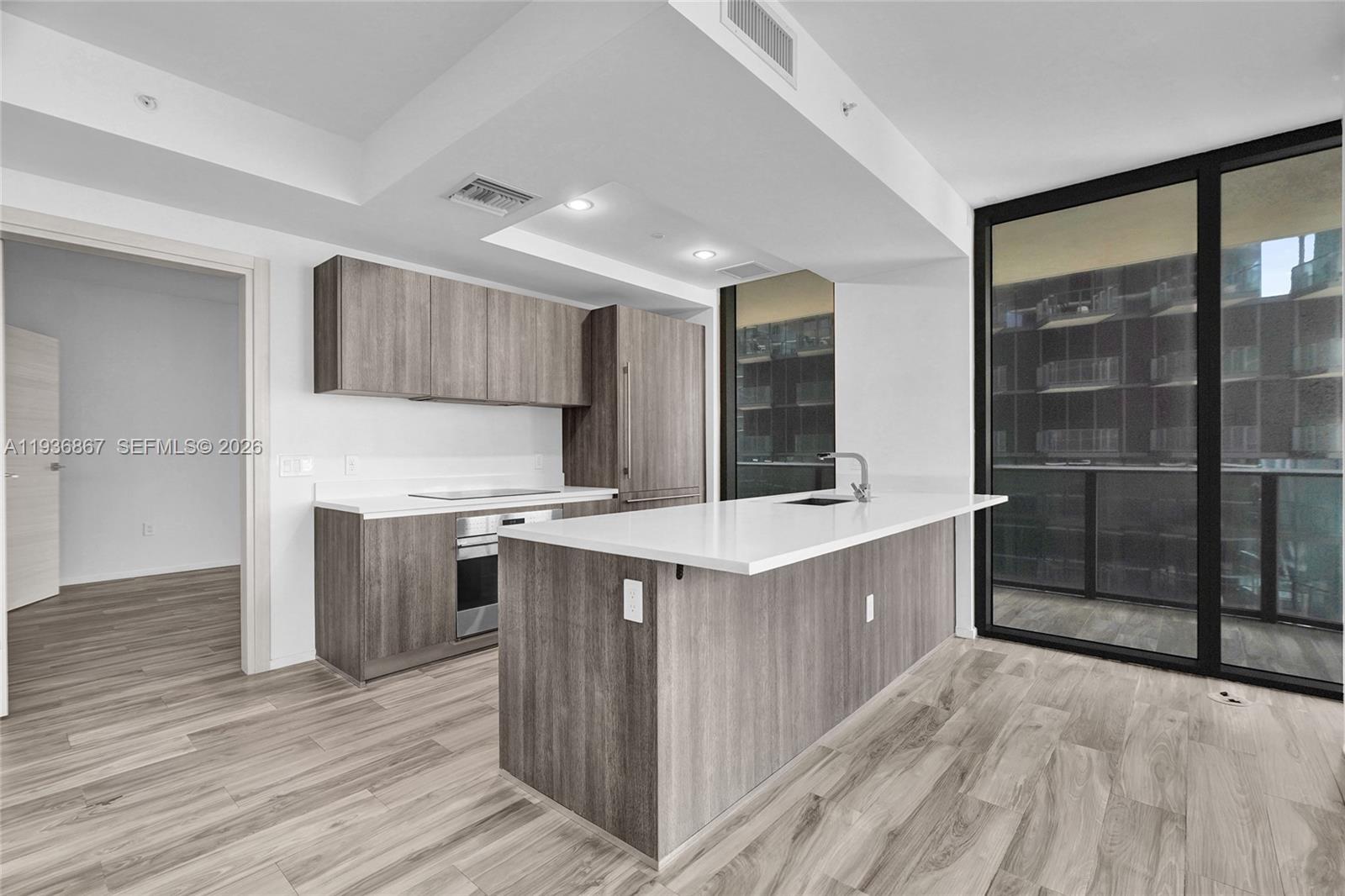 A modern kitchen features wood-grain cabinetry, white countertops, a central island, and floor-to-ceiling windows — 801 S Miami Ave # 2405, Miami FL 33130, MIAMI, FL