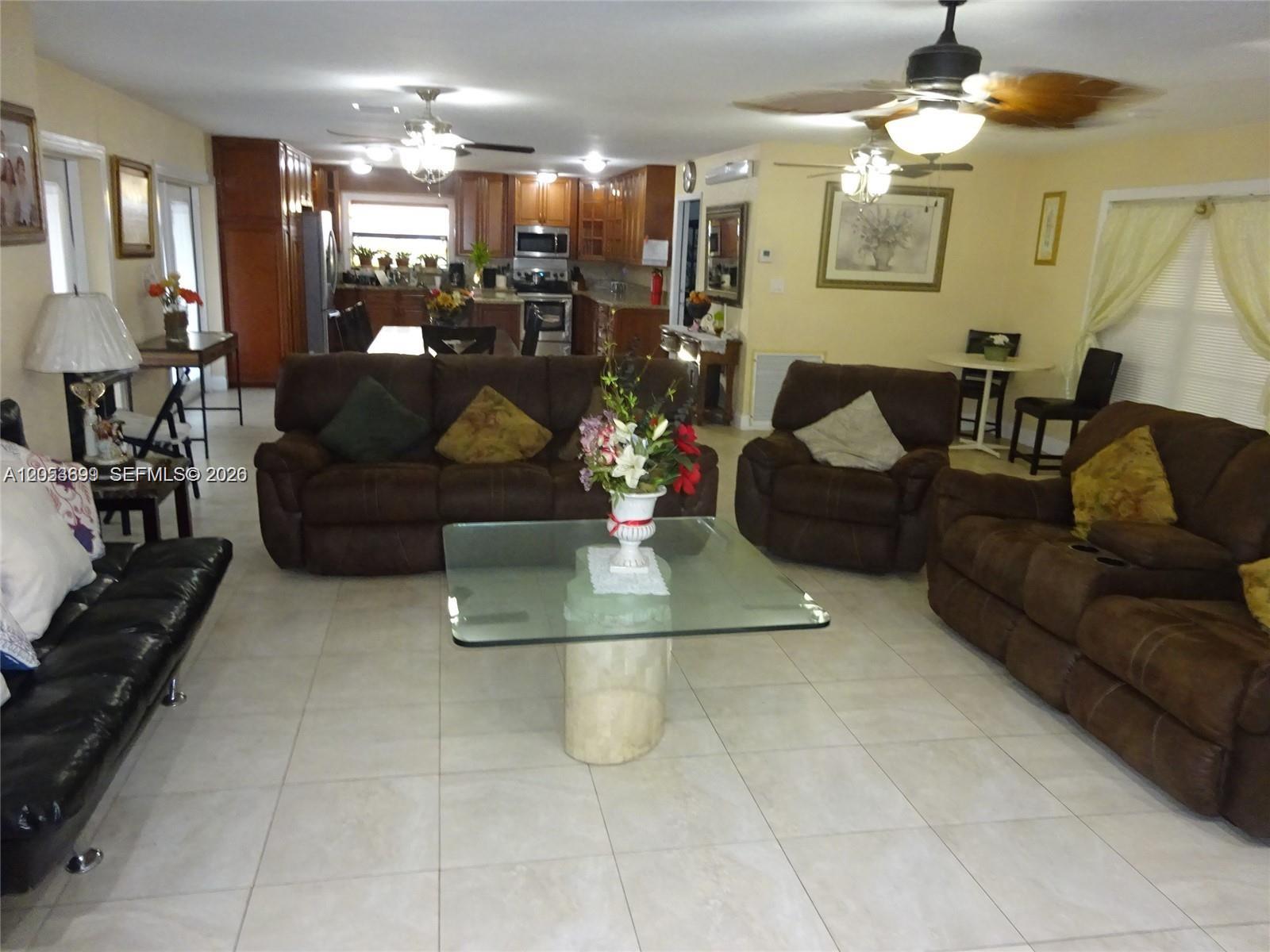A spacious open-concept living room features brown leather furniture, a glass coffee table, and tile flooring — 9240 SW 56th St # 0, Cooper City FL 33328, COOPER CITY, FL
