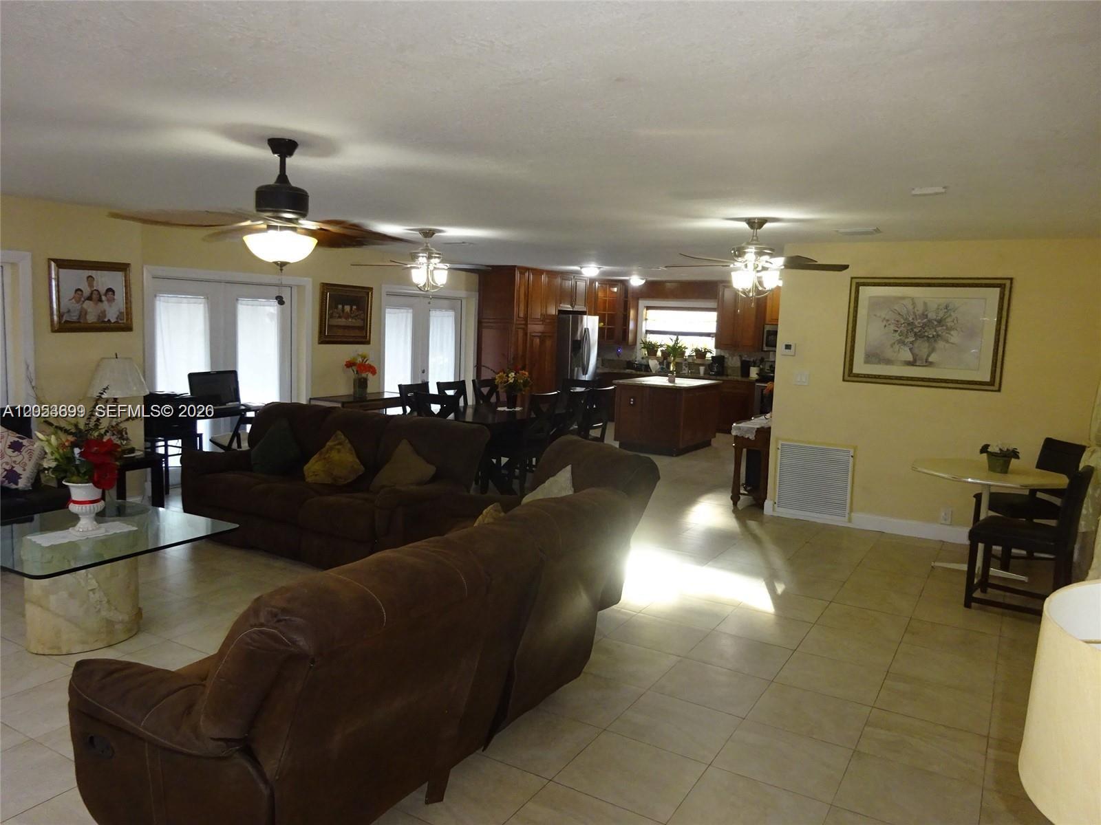 An open-concept living room and kitchen feature tile flooring, brown sofas, and wooden cabinetry — 9240 SW 56th St # 0, Cooper City FL 33328, COOPER CITY, FL