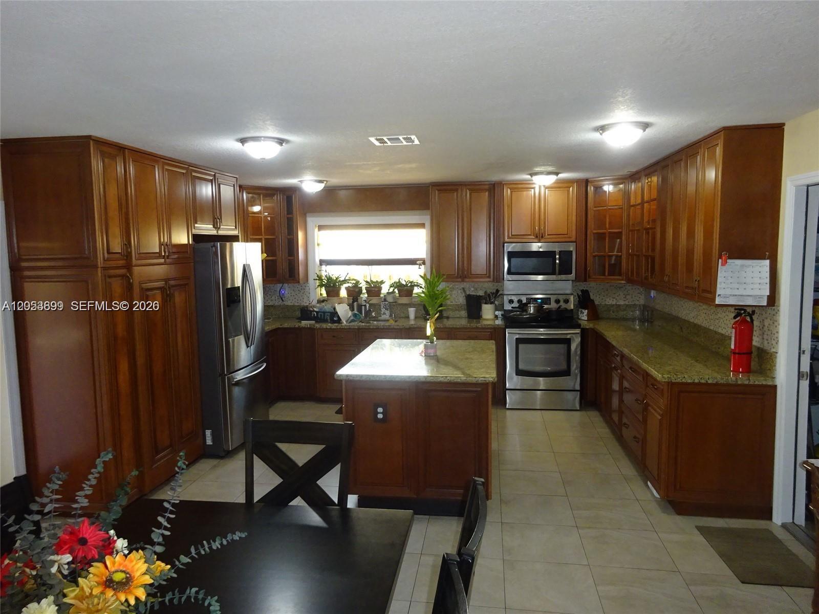 A kitchen features wood cabinetry, stainless steel appliances, a center island, and granite countertops — 9240 SW 56th St # 0, Cooper City FL 33328, COOPER CITY, FL