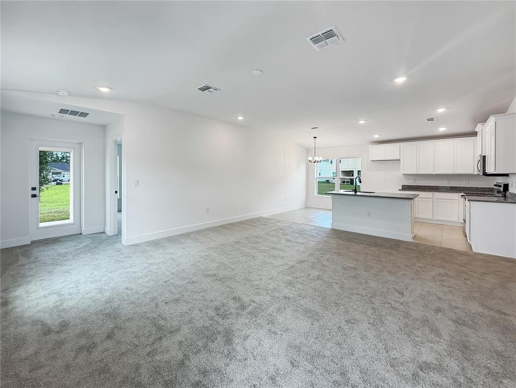 An open-concept living area features gray carpeting, white walls, and a kitchen with white cabinets — 3609 BRIARLYNNE WAY, ST CLOUD, FL