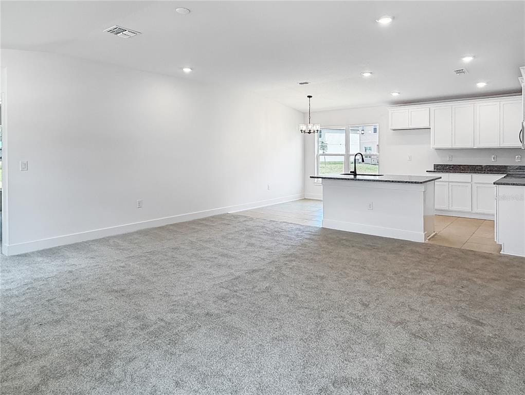 An open-concept living area features gray carpeting, a kitchen island, and white cabinetry — 3609 BRIARLYNNE WAY, ST CLOUD, FL