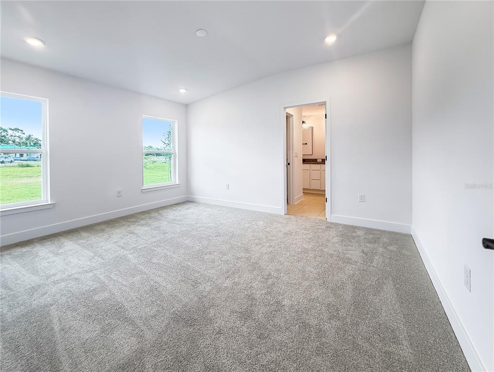 A carpeted bedroom with white walls, two windows, and an open doorway to a bathroom — 3609 BRIARLYNNE WAY, ST CLOUD, FL