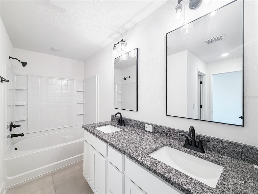 A bathroom features a double vanity with granite countertops, white cabinets, and a shower-tub combo — 3609 BRIARLYNNE WAY, ST CLOUD, FL