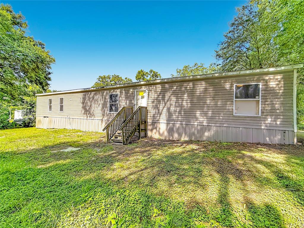 A single-story manufactured home with tan siding and wooden stairs sits on a grassy lot — 21420 NE 41ST STREET, WILLISTON, FL