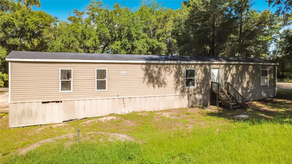 A tan mobile home with a dark roof sits on a grassy lot with trees — 21420 NE 41ST STREET, WILLISTON, FL