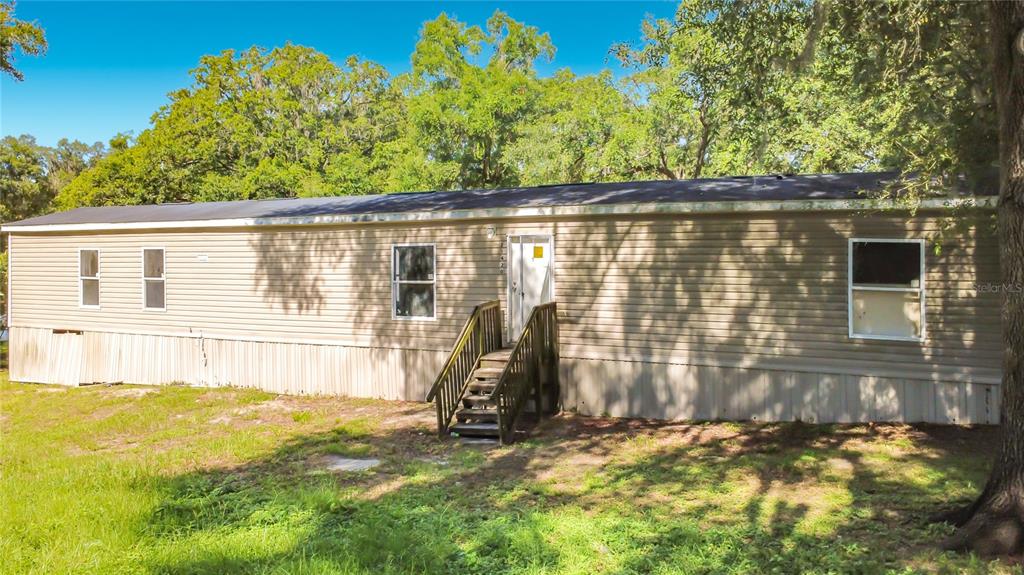 A single-story manufactured home with tan siding and wooden stairs sits on a grassy lot — 21420 NE 41ST STREET, WILLISTON, FL