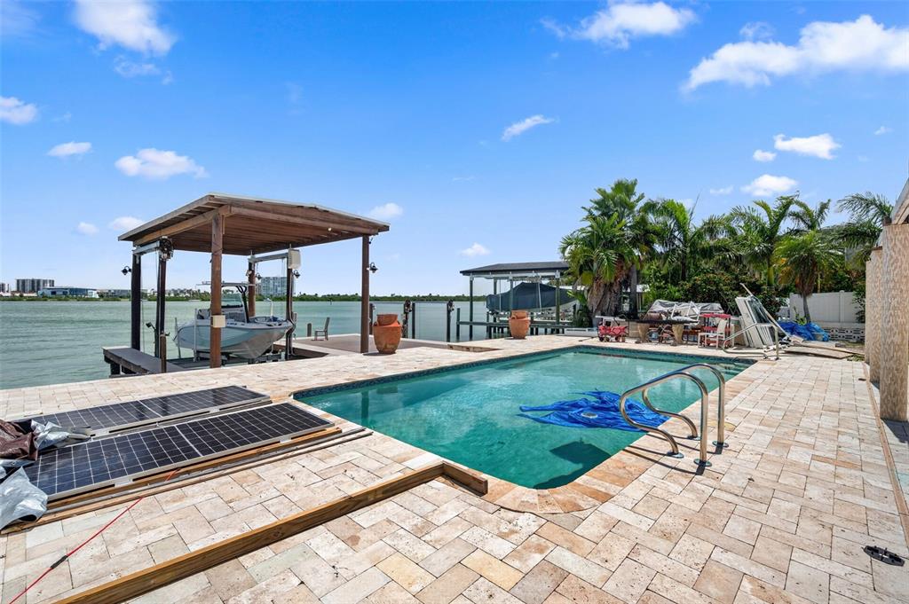 A swimming pool and boat lift sit on a stone patio overlooking the water — 246 BAYSIDE DRIVE, CLEARWATER BEACH, FL