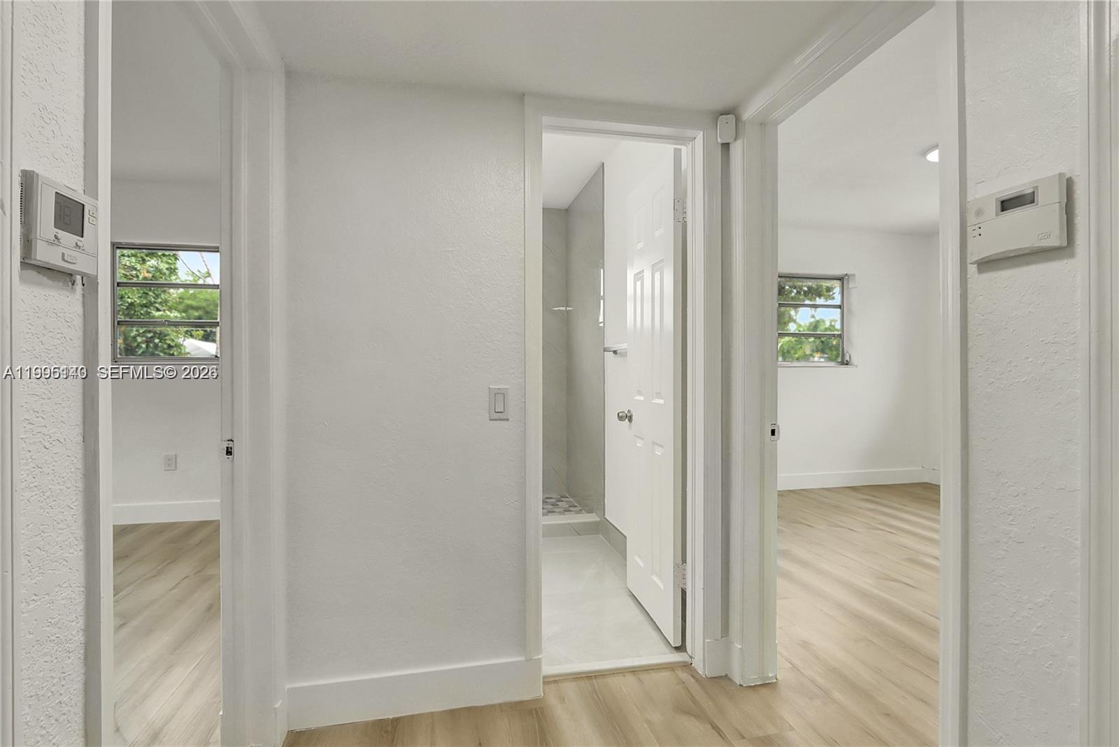 A hallway with light wood-look flooring leads to a bathroom and two adjacent bedrooms — 1340 NW 102nd St, Miami FL 33147, MIAMI, FL