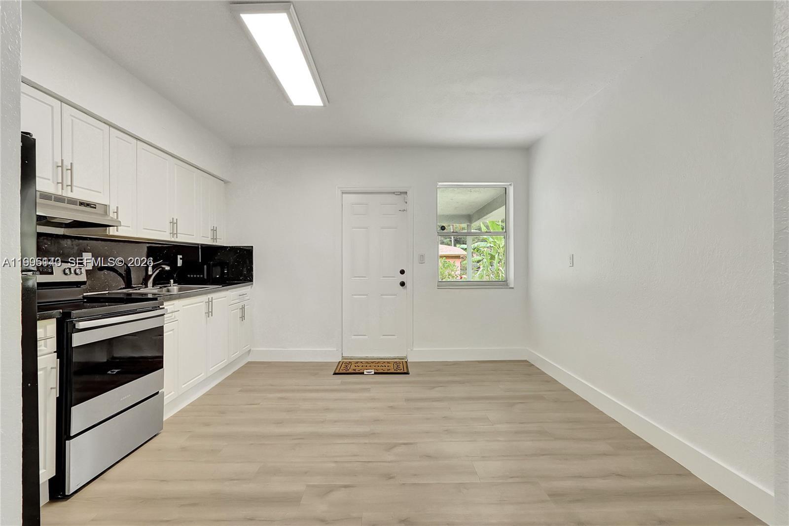 A kitchen features white cabinets, black countertops, stainless steel appliances, and light wood-look flooring — 1340 NW 102nd St, Miami FL 33147, MIAMI, FL
