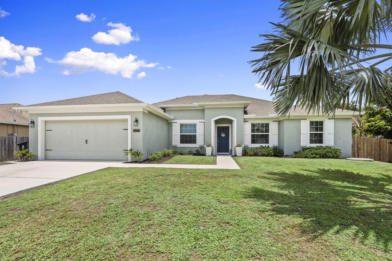 A light green single-story house with a two-car garage and a blue front door — 2141 SW Leafy Road, FL 34953, FL