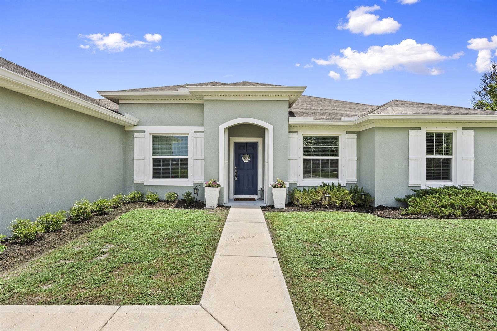 A light green single-story house features a dark blue front door and white shutters — 2141 SW Leafy Road, FL 34953, FL