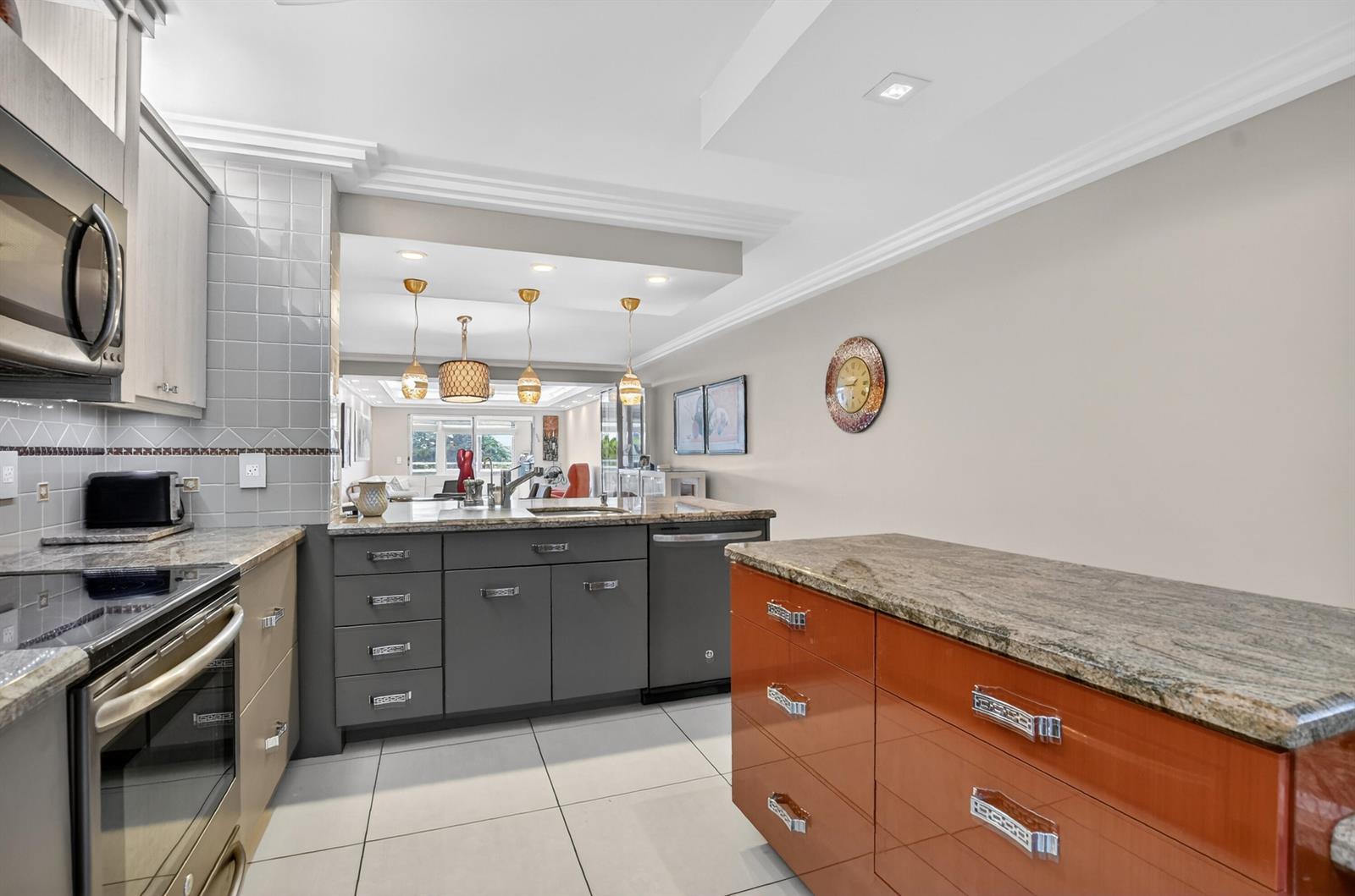 A kitchen features gray and orange cabinets, granite countertops, and a view into the living area — 3080 Yarmouth D, Boca Raton FL 33434, BOCA RATON, FL
