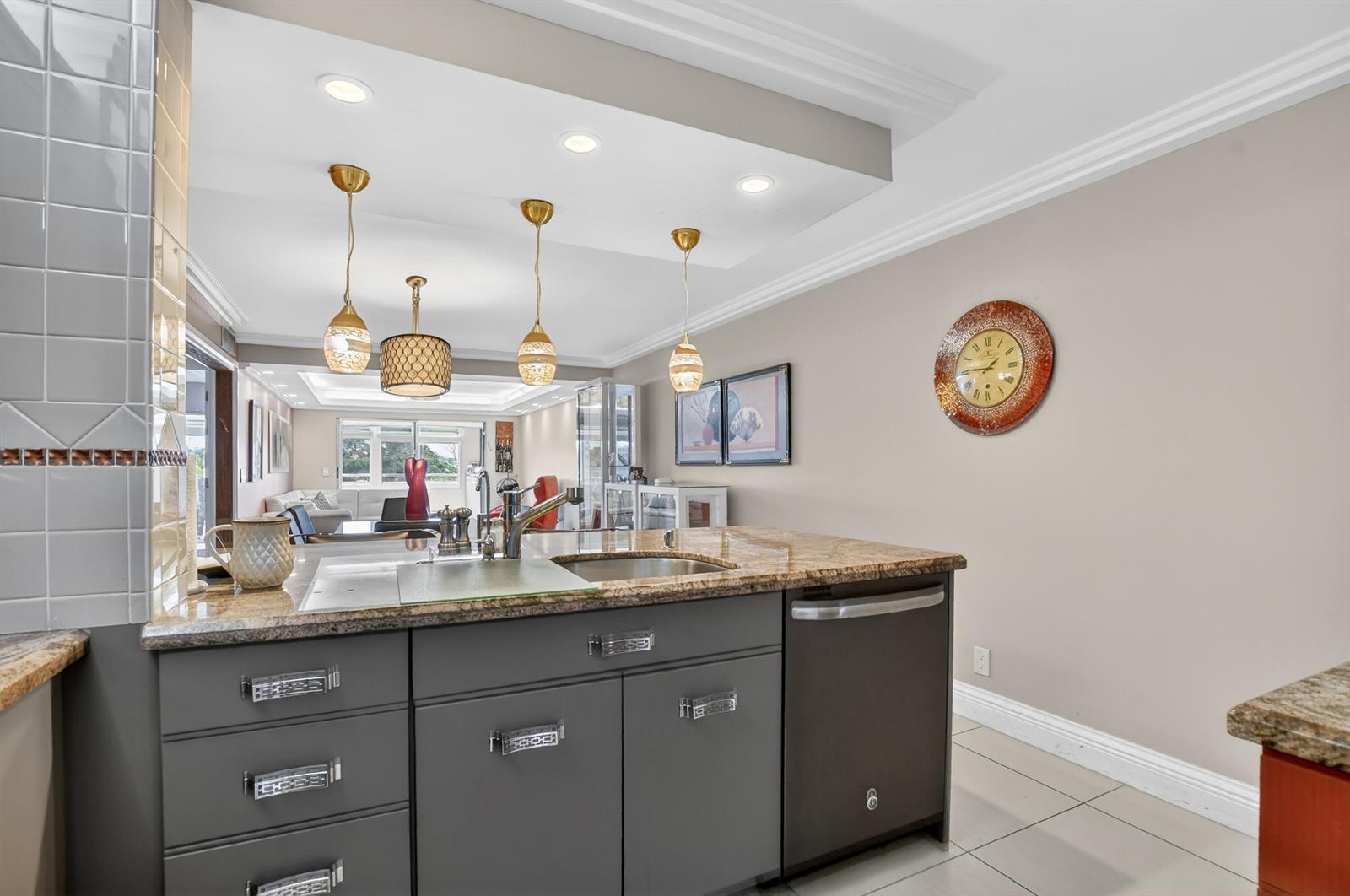 A kitchen island with gray cabinets and granite countertops sits in front of a living area — 3080 Yarmouth D, Boca Raton FL 33434, BOCA RATON, FL