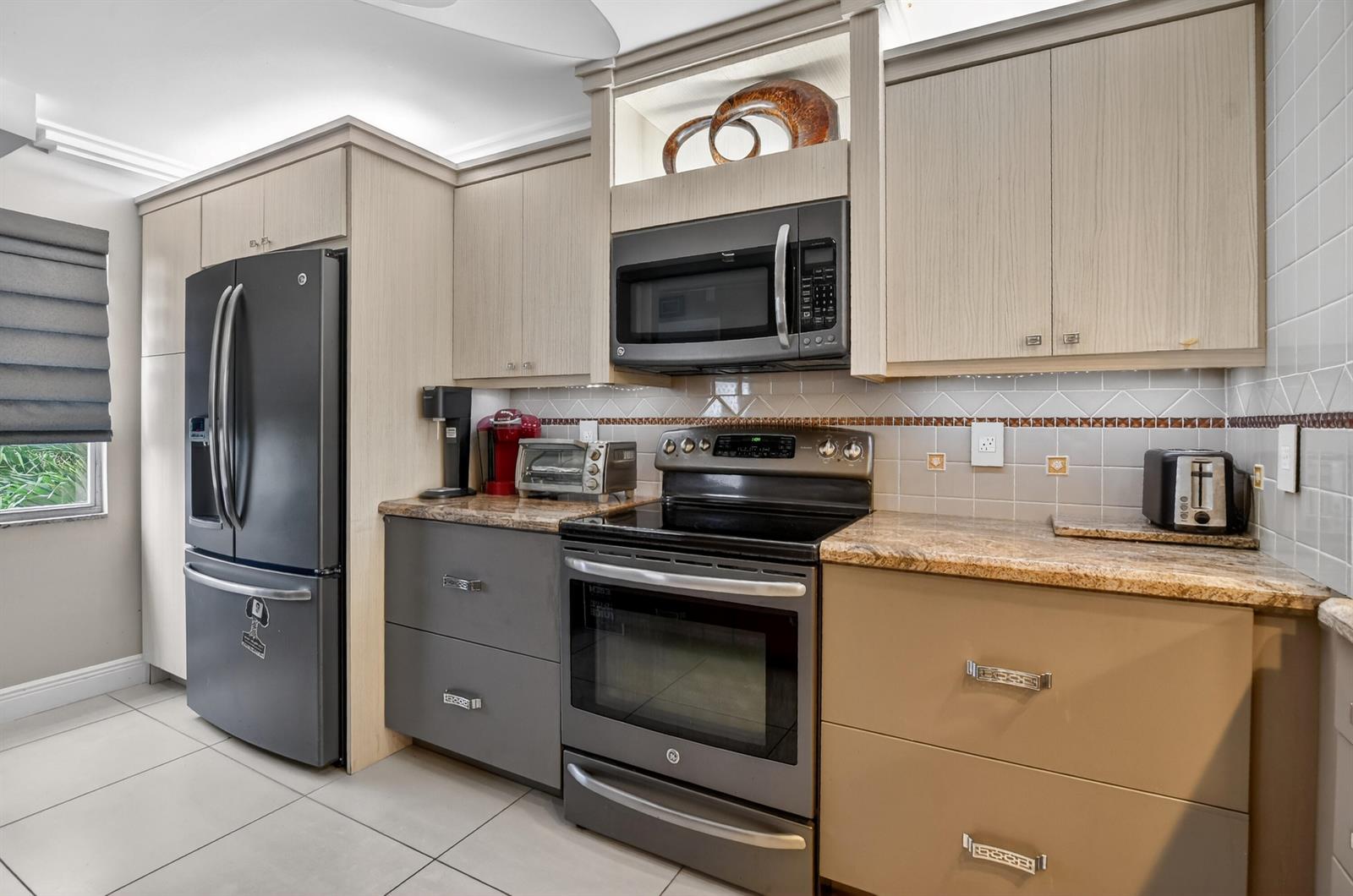 A kitchen features light wood cabinets, dark gray lower drawers, stainless steel appliances, and granite countertops — 3080 Yarmouth D, Boca Raton FL 33434, BOCA RATON, FL