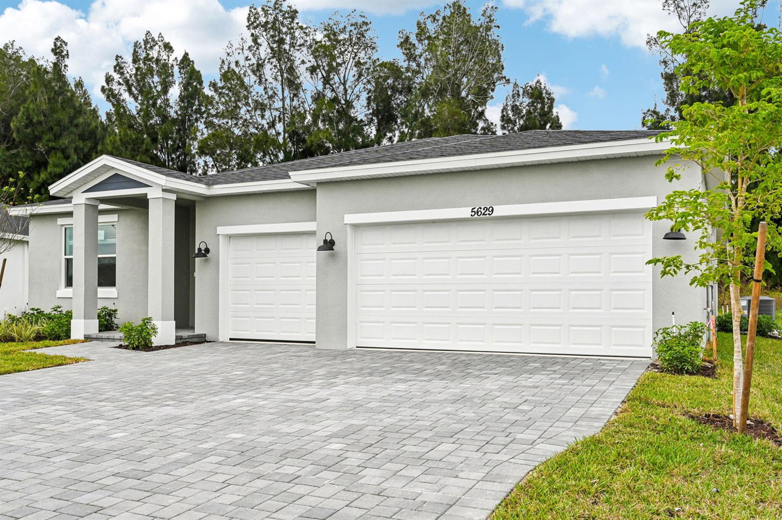 A light gray house features a paved driveway, two white garage doors, and a covered entryway — 5629 Hampton Park Circle, Vero Beach FL 32966, VERO BEACH, FL
